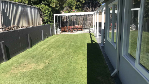 Mown lawn running along the side of a house in a fenced backyard