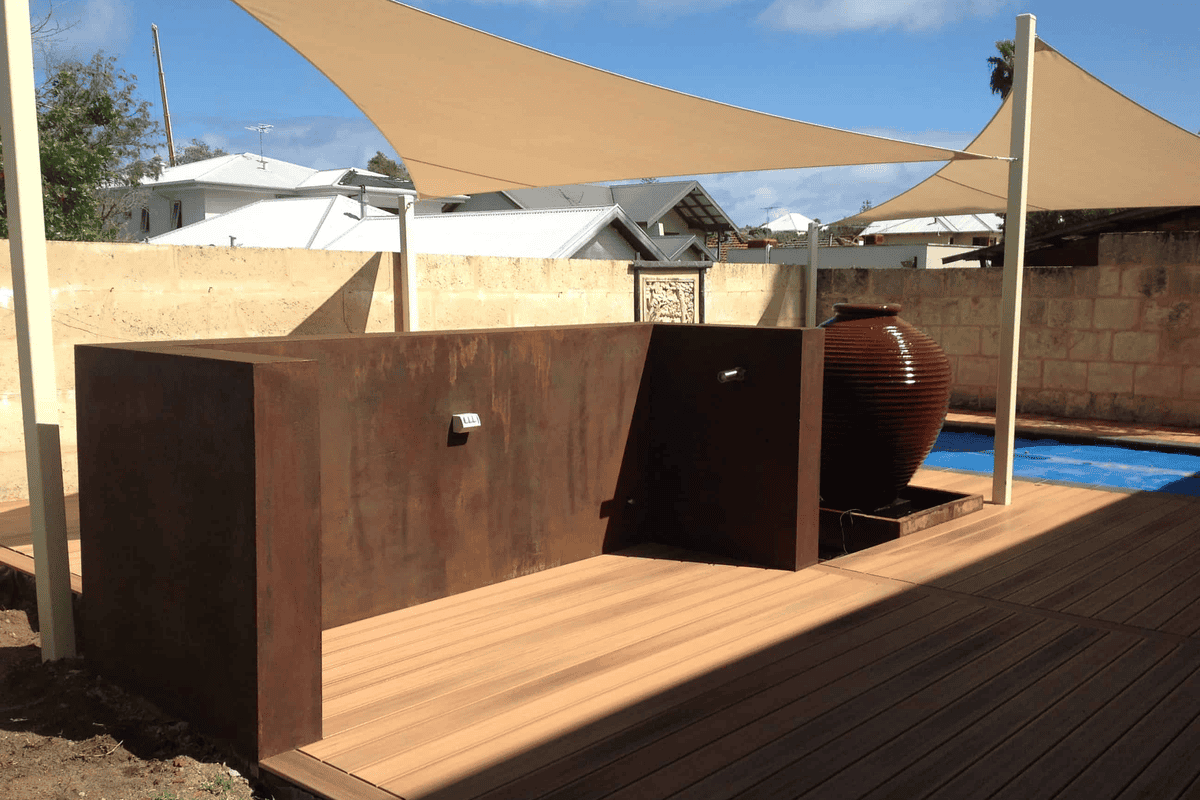 Small Perth backyard with a limestone wall, corten edging, paving and planted beds