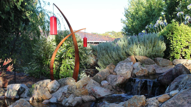 Rock waterfall and pond garden with a curved corten steel sculpture, lavender and silver-leaved plants