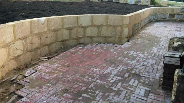 Curved retaining wall of pale stone blocks beside an area of brick paving